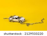 Small photo of Toy car model rewound by a steel chain on a yellow background. Driving license revocation concept