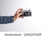 Man's hand in denim shirt holding retro film camera on gray background