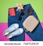Small photo of Women's accessories lie on classic jeans with an overstated waist. Sneakers, purse, bag, belt on a pink green background. Top view. The concept of travel.