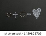 Small photo of Wedding rings and plus and heart drawing with calk on calkboard. Husband and wife or groom and bride, married couple concept.