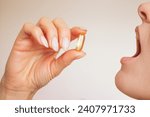 Profile of a young Caucasian brunette woman holds a pill with her fingers and puts it in her mouth. Taking medications and vitamins. Maintaining health. Omega 3. 