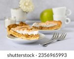 Two slices of pie with apple, cinnamon and meringue on saucers, forks and cups for coffee, a green apple and a vase with a flower.