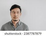 Small photo of Close up of Asian man with beard wear grey t-shirt emotionless face, looking at empty space isolated over white background wall.