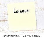 Small photo of Yellow sticky note on wooden wall with handwritten inscription heinous
