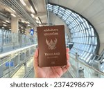 Small photo of BANGKOK, THAILAND - 13 Oct, 2023 : A hand holding a Thai passport before departure at Suvarnabhumi Airport. Thai tourist is preparing for holiday flight.