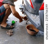 Small photo of Magetan 8 September 2023 A man wearing a black and red shirt with brown skin is opening motorbike oil at a workshop on Jalan Ponorogo Magetan. There is also oil in a green plastic funnel wearing sanda