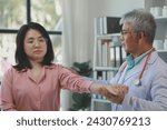 Small photo of A young Asian female patient is being examined by a medical professional, A dignified middle-aged male doctor is diagnosing a patient's body in order to plan a treatment.