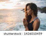 Small photo of Young woman praying and meditating alone at sunset with beautiful ocean and mountain view. Self-analysis and soul-searching. Spiritual and emotional concept. Introspection and soul healing.