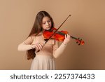 Small photo of Portrait of a girl with a violin and a bow in her hands on a plain beige background. Music concept
