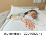 Small photo of Young patient asian woman lying on bed in hospital with IV saline drip to back of the hand, teenager sick in hospital, Selective focus, healthcare and health insurance concept.