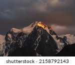 Small photo of Darkness mountain landscape with great snowy mountain lit by dawn sun among dark clouds. Awesome alpine scenery with high mountain pinnacle at sunset or at sunrise. Big glacier on top in orange light.