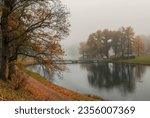 Small photo of Soft focus. Foggy melancholic autumn city park. Bridge over a pond duing a foggy morning. Gatchina, Palace Park, Russia.