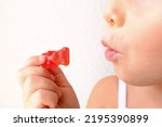 Small photo of small child, blonde girl 3 years old wants to eat gelatinous sweets, holds in her hands gummy bear, kid has a good appetite, happy childhood, balanced diet, sweet life, unhealthy food, halal food