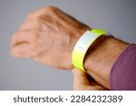 Small photo of close-up of neon yellow paper bracelet on the male arm of adult clinic patient, check tape with entry number on hand of middle-aged european man, event ticket concept