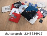 Small photo of vintage retro electronic data storage devices from the 80s, 90s, cd disk, flash drives, modern hard disk scattered on table. Stack of floppy disks in grey, black, blue, yellow, red, white