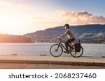 Small photo of White Caucasian Adult Woman riding a bicycle on Seawall in Stanley Park. Sunset Sky Art Render. Downtown Vancouver, British Columbia, Canada.