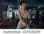 Small photo of Fit young African American female athlete in sportswear exercise bodybuilder pulling down wire cable on gym equipment in fitness center.Workout for good health concept.
