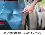 Small photo of Driver hand examining dented car with damaged fender parked on city street side. Road safety and vehicle insurance concept