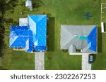 Small photo of Aerial view of damaged in hurricane Ian house roofs covered with blue protective tarp against rain water leaking until replacement of asphalt shingles