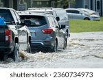 Small photo of Flooded town street with moving cars submerged under water in Florida residential area after hurricane Ian landfall. Consequences of natural disaster