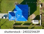 Small photo of Top view of leaking house roof covered with protective tarp sheets against rain water leaks until replacement of asphalt shingles. Damage of building rooftop as aftermath of hurricane Ian in Florida
