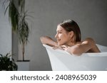 Small photo of Happy, dreamy girl with haircut resting in bathtub, enjoying pastime in spa. Close up of relaxed caucasian woman leaning, putting crossed arms on bath edge and smiling. Wellness, spa concept.