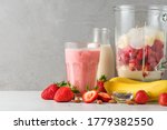 Glass strawberry and banana smoothie or milkshake with fresh juicy ingredients in blender for making healthy drink. Cooking concept