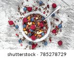 homemade chocolate muesli or granola in a bowl with a spoon, berries, dried fruits and nuts. healthy breakfast. top view