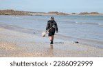 Small photo of A view of a solitary beachcomber at the waters edge, Saint-Jacut-de-la-Mer, Brittany, North West France, Europe on Good Friday, 7th, April, 2023