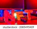 NFT ( Non-Fungible Token ) text of letters illuminated with neon light. Workplace of a graphic designer creating NFT digital art. Concept of cryptoart and blockchain technology
