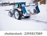 Rear view of blue tractor with loader and snow chains clearing snow.  Winter landscape