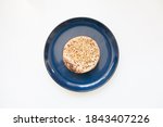 Small photo of Top down view of a single English crumpet on a plate against a white background. The baked breakfast cake is full of holes.