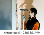 Small photo of middle-aged man chipping away at the wall of a house with a large sledgehammer for home renovation work