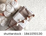 Small photo of Well groomed woman hand holding a cotton branch with stack of neatly folded linens near rolled up towels in mesh basket placed on knitted chunky merino wool yarn plaid. Natural textile. Top view.