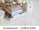 Well groomed woman hands holding the cotton branch with pile of neatly folded bed sheets, blankets and towels. Production of natural textile fibers. Manufacture. Organic product.