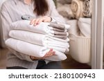 Beautiful woman in winter thick warm robe is sitting and neatly folding bed linens and white bath towels. Organizing and sorting clean laundry. Organic and natural cotton textile. Manufacture.