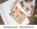 Small photo of Childish hands holding alphabet wooden board with colored font letters in cells closeup. Boy girl kid arms intellect game playing early development primary education letters learning