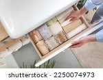 Small photo of Top view of woman hands neatly organizing bathroom amenities and toiletries in drawer or cupboard in bathroom. Concept of tidying up a bathroom storage by using Japanese method.