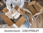 Small photo of Woman packing clothes and shoes into cardboard box seasonal comfortable storage organize top view closeup. Female with container for wardrobe keep for donation charity online shopping order moving