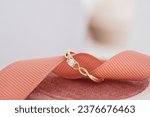 Small photo of Exquisite gold ring with a sparkling diamond, intricately designed with a heart motif, elegantly placed on a salmon-colored textured ribbon atop a velvety surface.