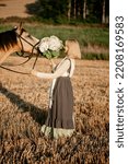 Small photo of A young woman walking through a field in the summer in the village met a prodigal horse and decided to pet him.