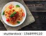 Spaghetti bolognese
served on a white plate on a dark wooden background with tomatoes and basil