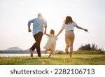 Small photo of Happy family in the park sunset light. family on weekend running together in the meadow with river Parents hold the child hands.health life insurance plan concept.