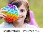 Small photo of Close up of portrait little girl with a modern popit toy. Colorful and bright pop it toy simple dimple. Trendy antistress sensory toy fidget push pop it and simple dimple in kid's hands