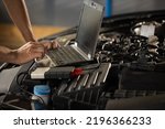 Automobile service, car mechanic. Auto mechanic uses a laptop while conducting diagnostics test. Specialist inspecting the vehicle in order to find broken components and errors in data logs.