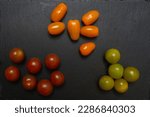 Small photo of Three groups of different cherry tomatoes on clack stone plate. Top view composition.