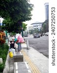 Small photo of 30 December 2023, Yogyakarta, Indonesia: an old woman with white hair carrying a large bag on her back works as a scavenger and is seen scavenging for rubbish in a roadside trash can in the morning