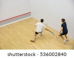 Squash players in action on squash court, back view/Two men playing match of squash.