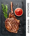Small photo of tomahawk beef steak grilled with spices on stone background