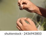 Small photo of Closeup of hand baiting a fishing hook, Uses worms as fishing bait.